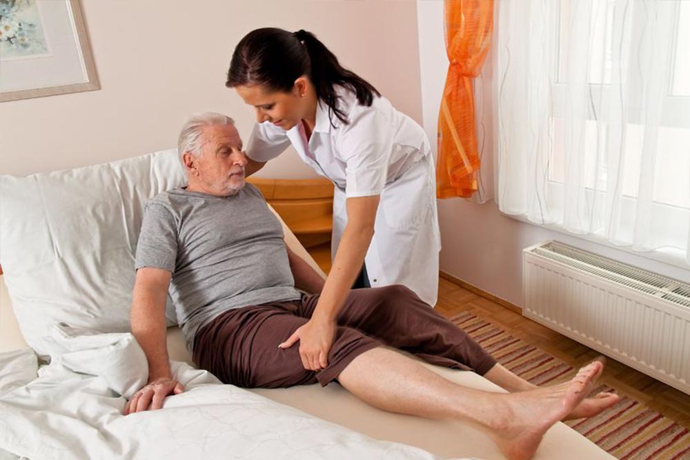 Young nurse helping a senior male patient to rise from his bed.