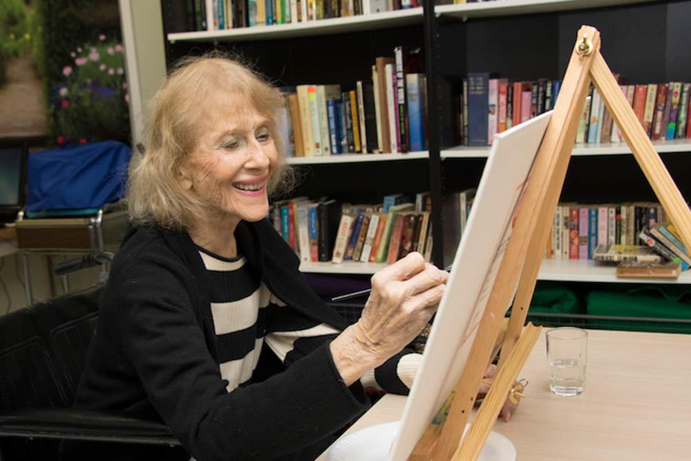 Senior woman smiling while painting on canvas.